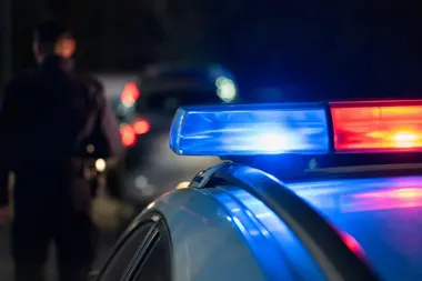 Nocna akcja policyjna: w pierwszym planie światła błyskowe radiowozu, w tle stoi funkcjonariusz przy zaparkowanych samochodach.